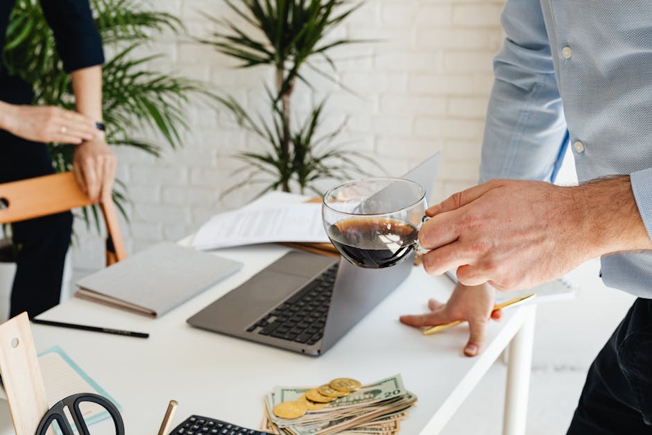 Two people working at an office desk with coffee, laptop, and financial documents.